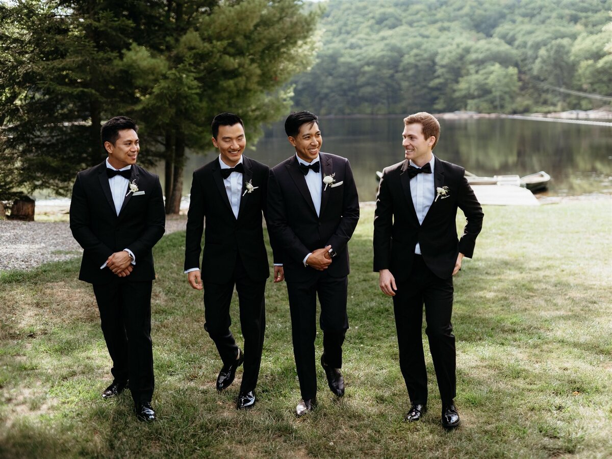 Groom and groomsmen walk outside on the grass in front of lake and trees at Cedar Lakes Estate in Hudson Valley