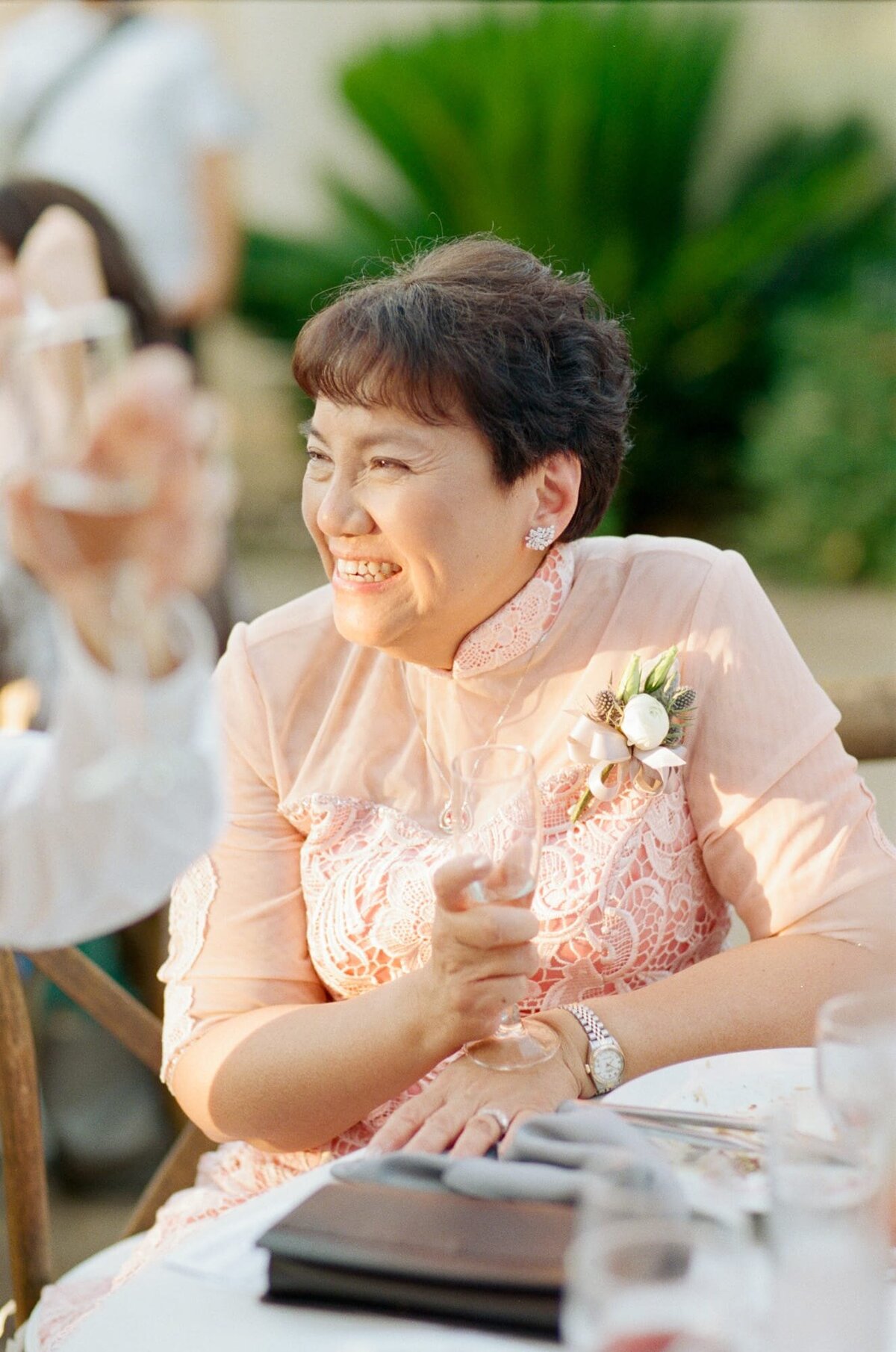 Mother of the bridegroom in pink attire watches intently at her son's wedding.