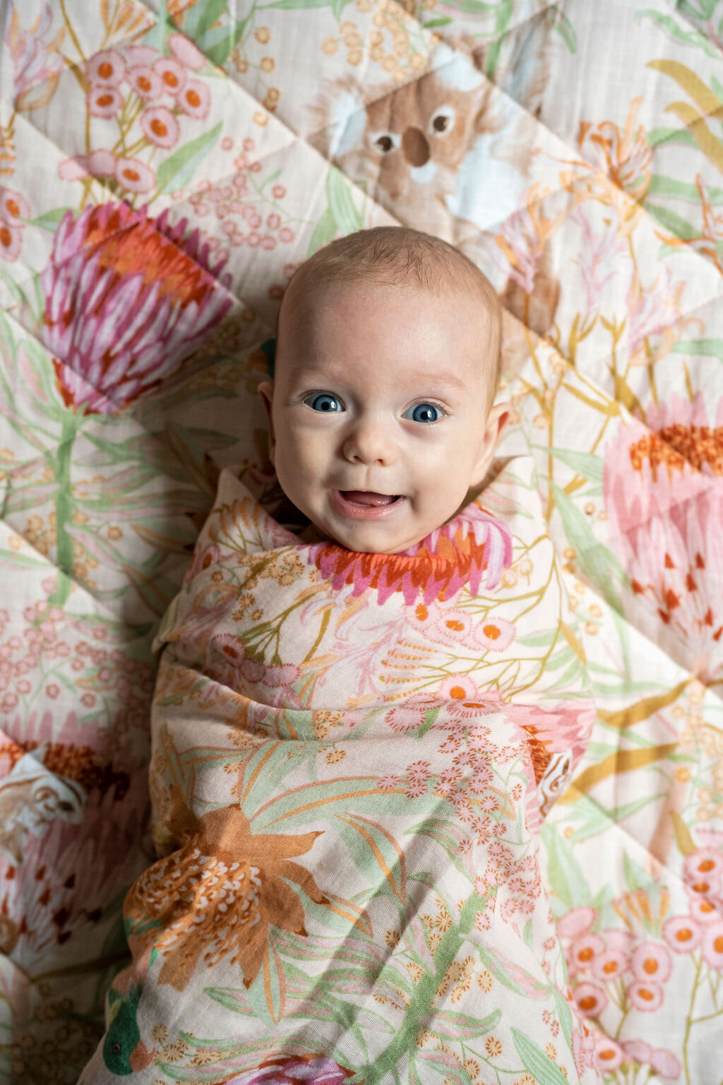 Newborn baby girl swaddled and smiling at the camera during an at home photo shoot