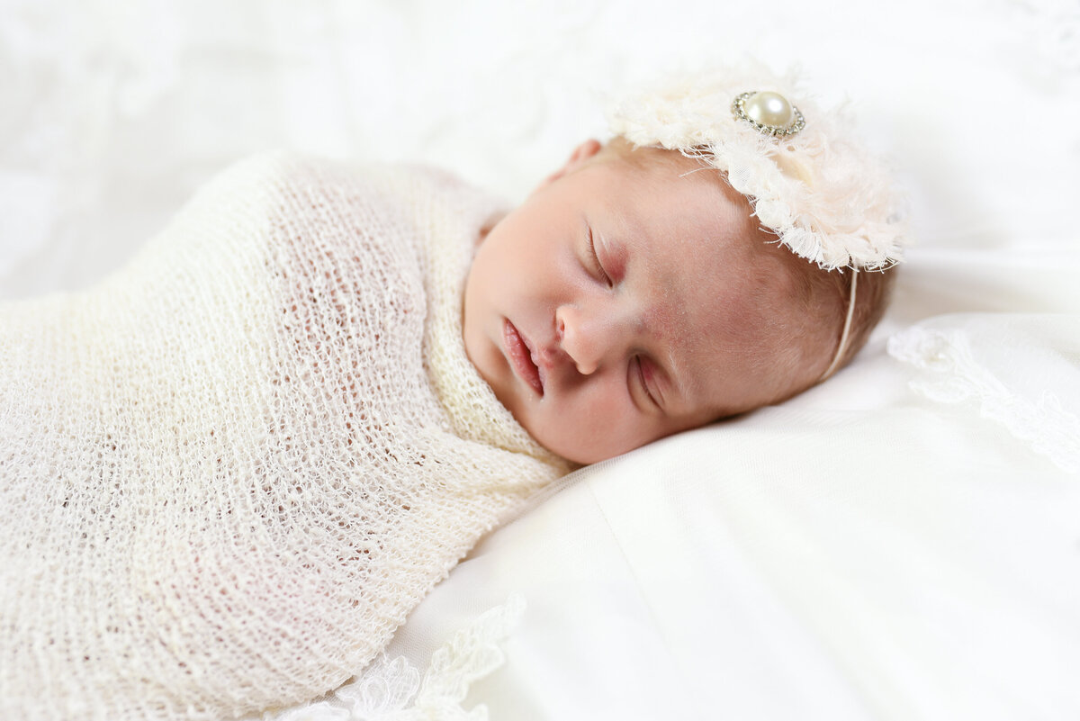 Beautiful Mississippi newborn photography: Baby girl wrapped in white with rhinestone headband on mom's wedding gown