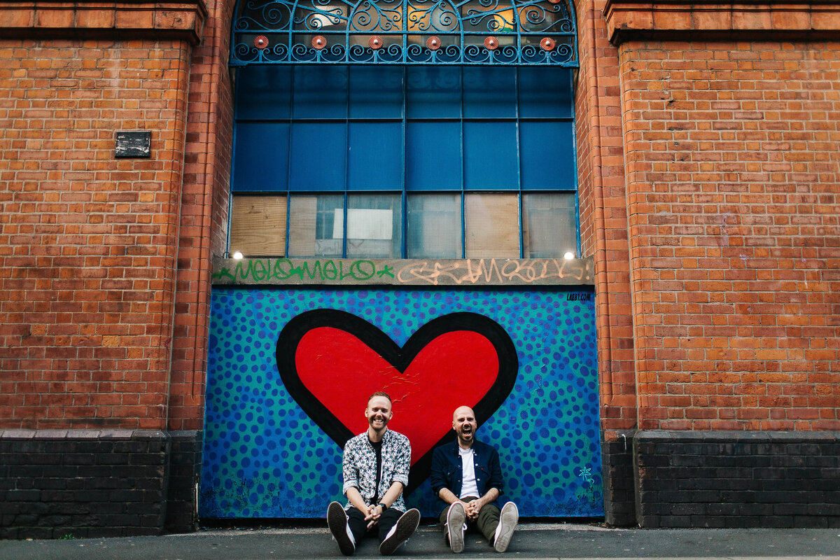 A gay couple on their Love Shoot sat down in front of a huge street art love heart in Manchester
