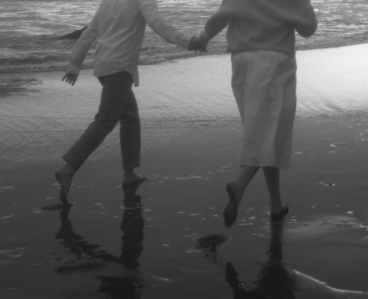 Black and white dreamy photo couple running away on beach