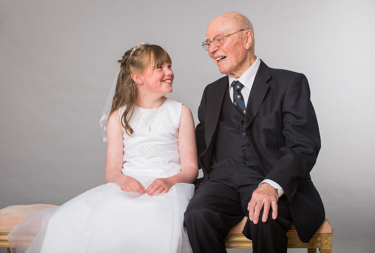 portrait of a girl in white communion dress smiling at her grandfather