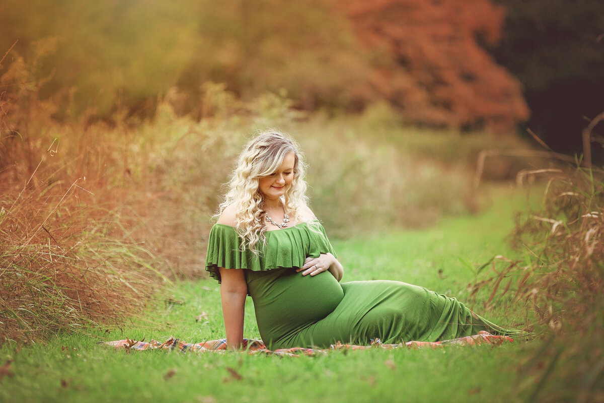 expecting mom sitting in the grass wearing a green dress showing off her belly
