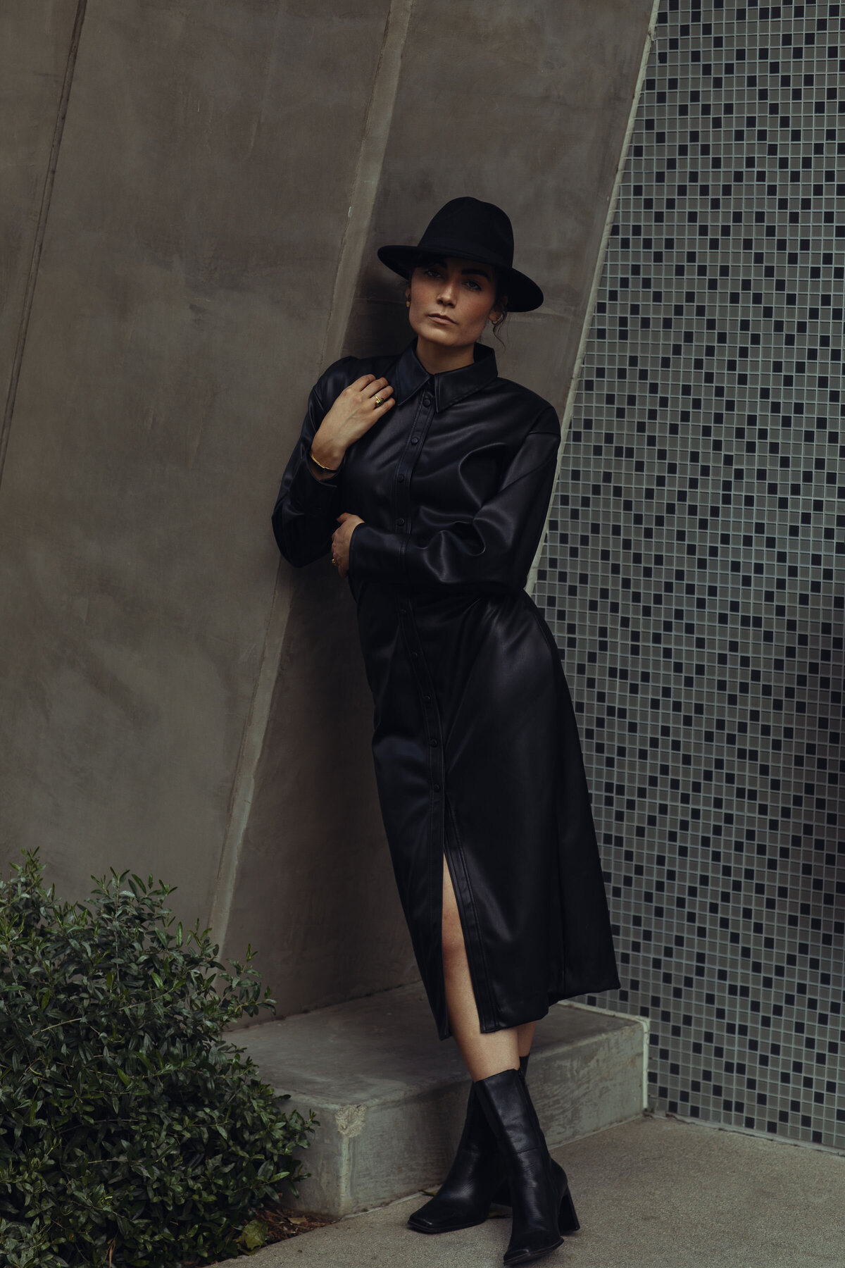 Portrait Photo Of Young Woman In Black Coat And Black Boots Leaning Against a Wall Los Angeles