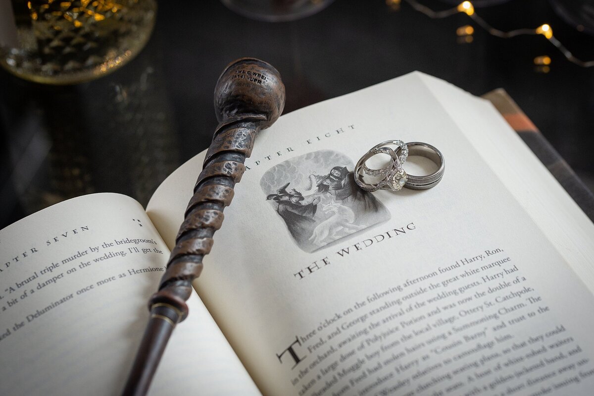 Harry Potter and the Deathly Hallows novel opened to The Wedding chapter with a wood carved wand and a set of platinum wedding bands with a solitaire diamond engagement ring for a Harry Potter wedding in Nashville.