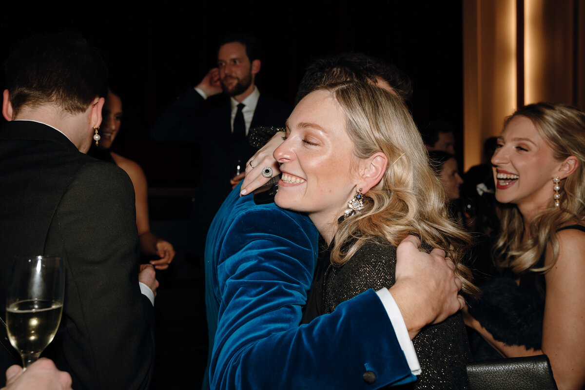 A woman hugs the groom in blue velvet suit at their wedding reception.