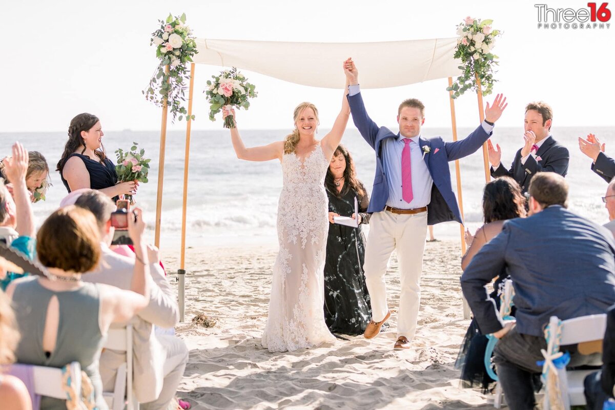 Bride and Groom raise their hands in the air as they face their wedding guests