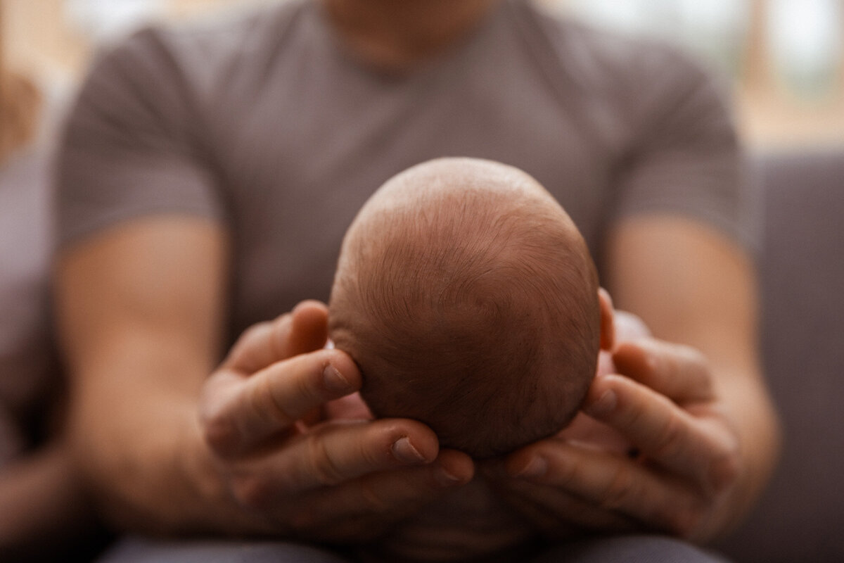 Detaljbilde av babyens hode som ligger i fars hender.