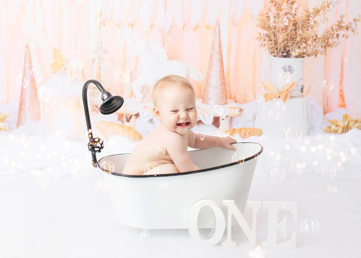 Baby in a bath for splash time after her cake smash photoshoot and laughing - By Los Angeles Newborn Photographer