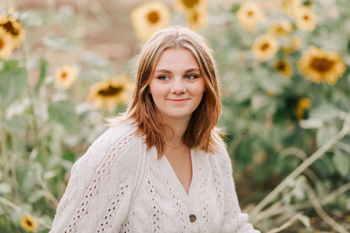 A girl in a white sweater sits in a sunflower field