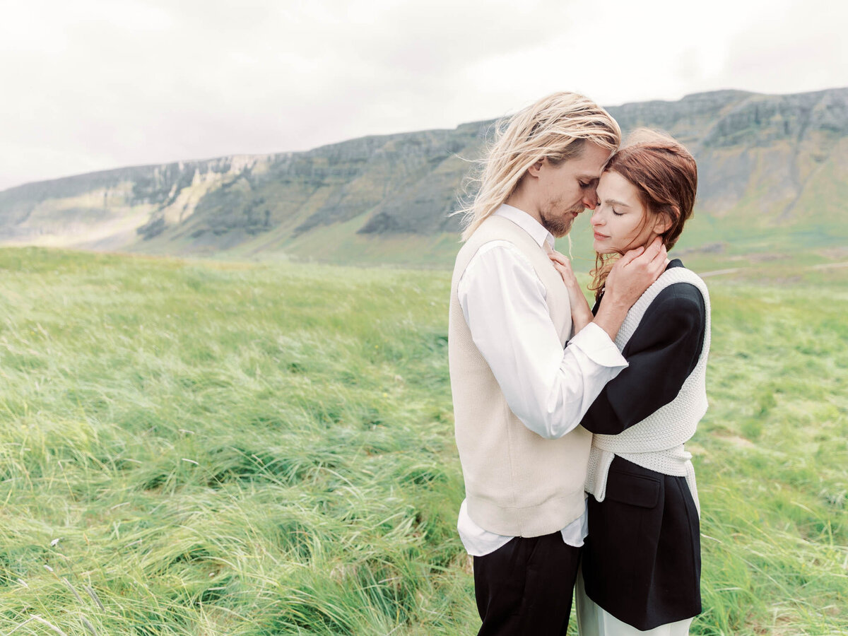 An engaged couple wearing black and white Ralph Lauren stylish clothes hugging each other in a breathtaking landscape of iceland with long grasses