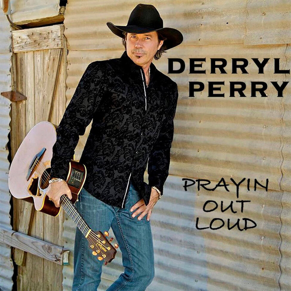 Country Music Single Cover Title Prayin Out Loud Artist Derryl Perry leaning against wood wall holding acoustic guitar by neck wearing black shirt blue jeans black cowboy hat