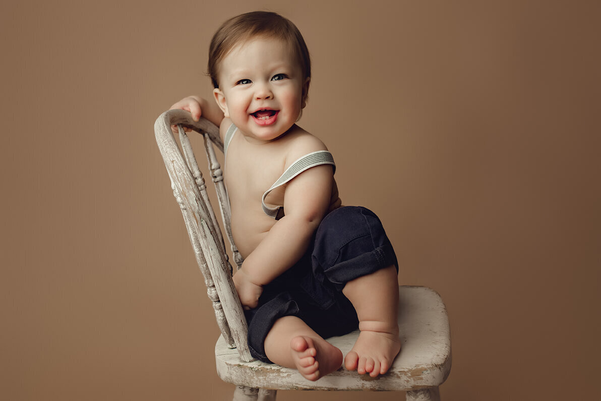 six month old boy sitting in a white chair laughing