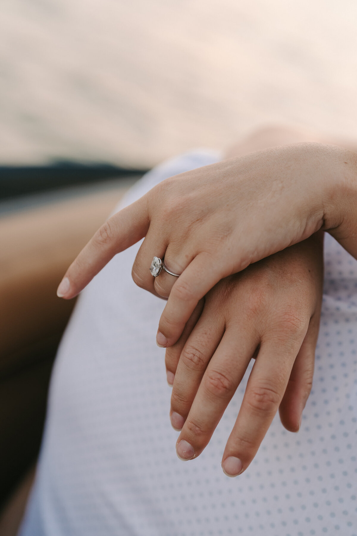 A photograph in color of Jessica and Jeff during their engagement session on a boat on Lake Travis in Austin, Texas. The photograph shows a close-up of Jessica’s hands around Jeff’s neck. Her hands are relaxed, crossed at the wrists, and her engagement ring is sparkling. Wedding and engagement photography by Stacie McChesney/Vitae Weddings.