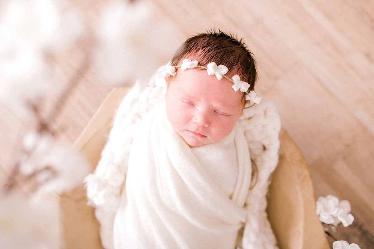 Baby wrapped in white cloth with white flowers around her