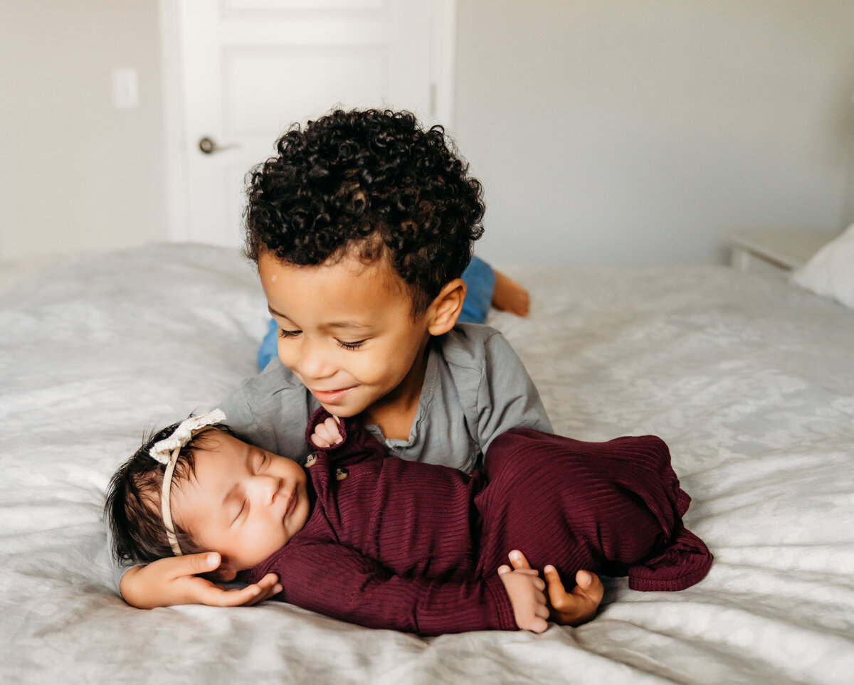 Newborn Photographer, baby sisters lays asleep, older brother crawls over to hold her