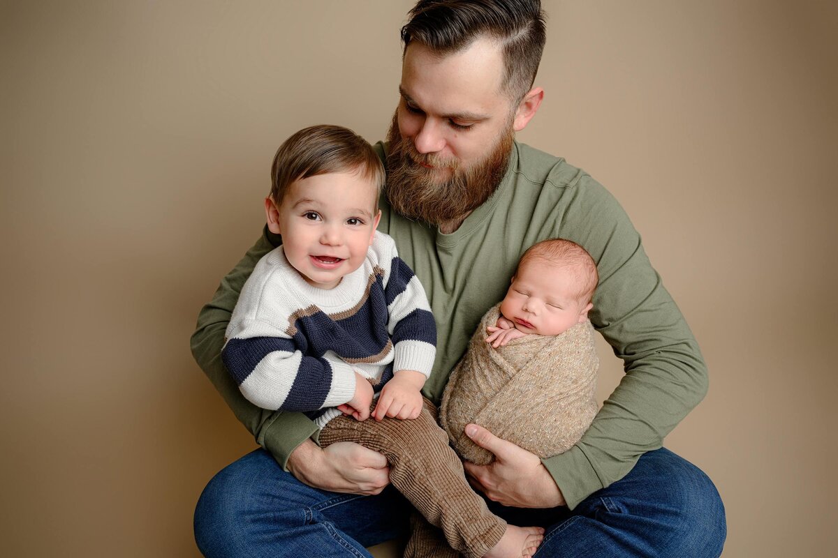 father looks down at his toddler son in his lap while hold both his sons 