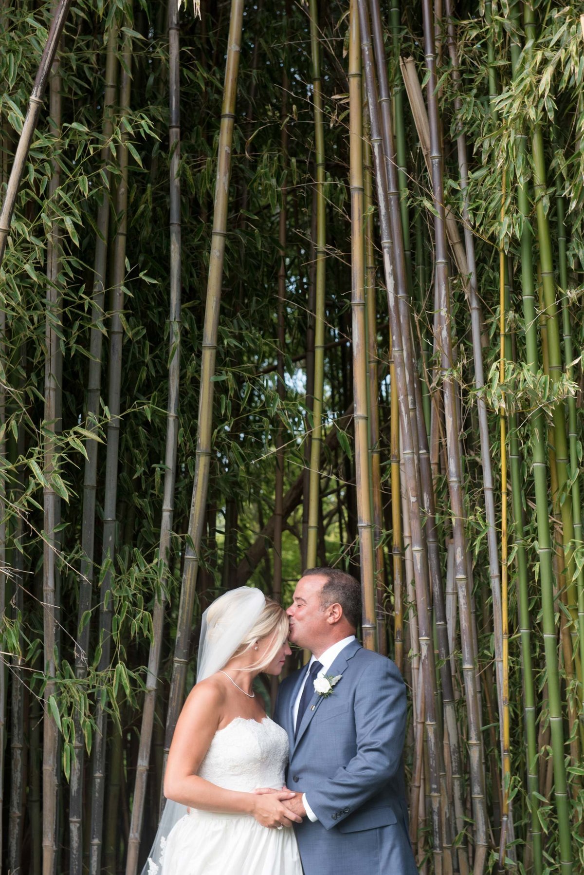Groom kissing bride outside in front of trees at Huntington Crescent Club