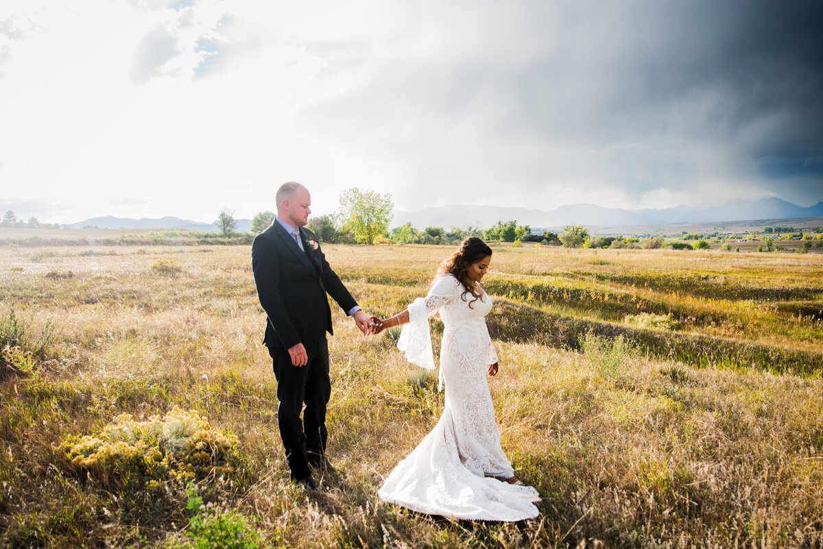 A bride leads her groom through a field at golden hour.