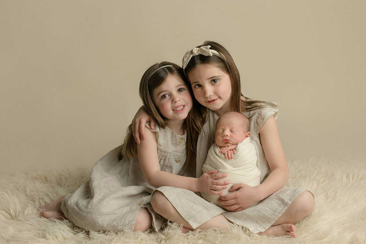 Two older sisters holding newborn brother during newborn photography session