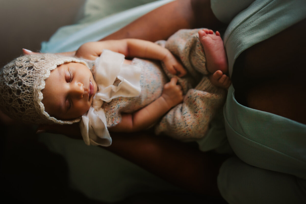 sleeping newborn girl laying on her mothers lap wearing a boho bonnet and crochet bodysuit