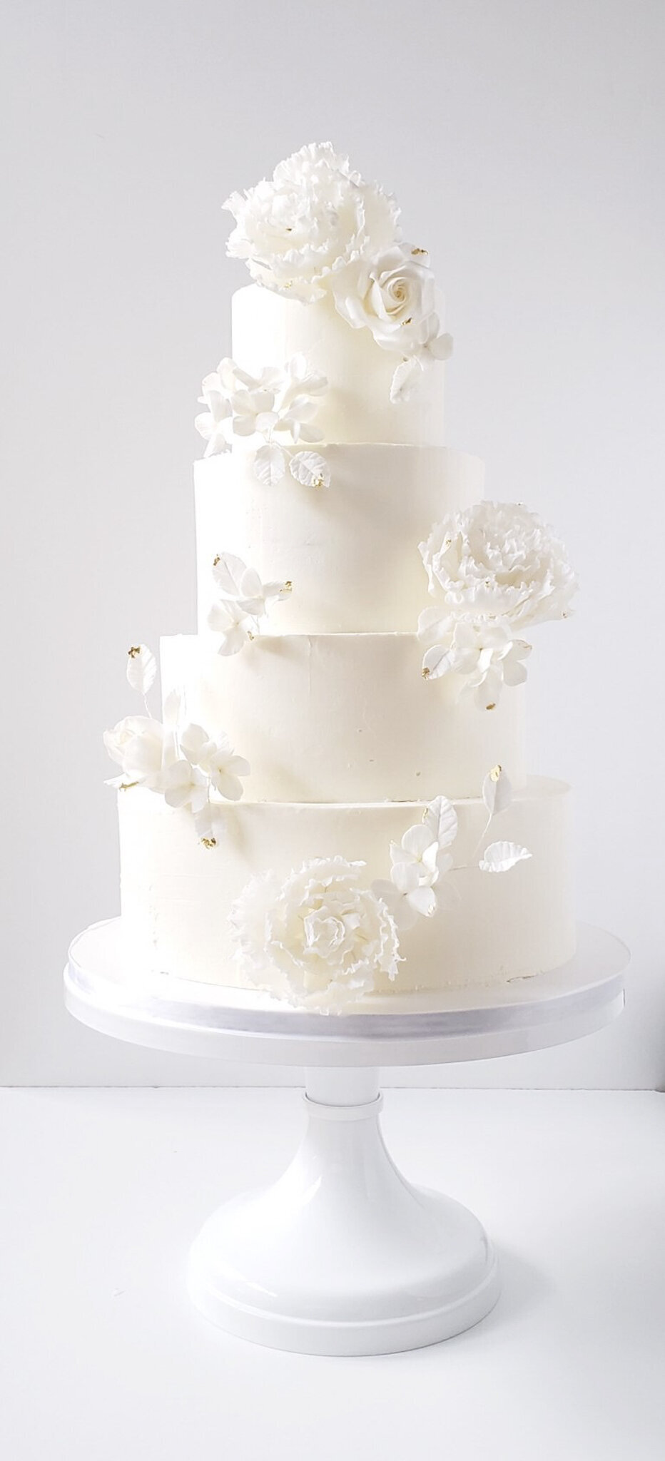 Elegant and timeless four-tiered white wedding cake, decorated with classic white sugar roses, created by Brianne Gabrielle Cakes,  elegant cakes & desserts in Edmonton, AB, featured on the Brontë Bride Vendor Guide.