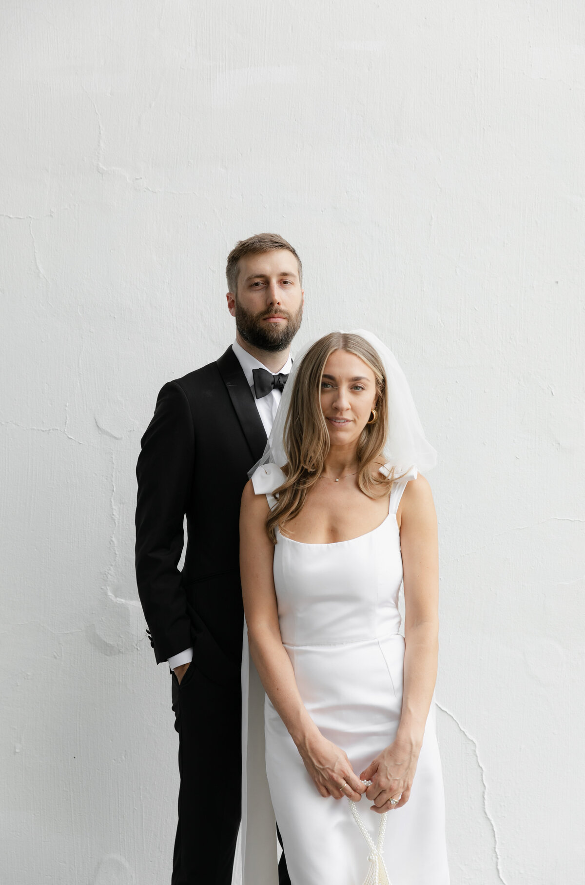 Bride and groom stand in front of white wall at Elske restaurant, Chicago.