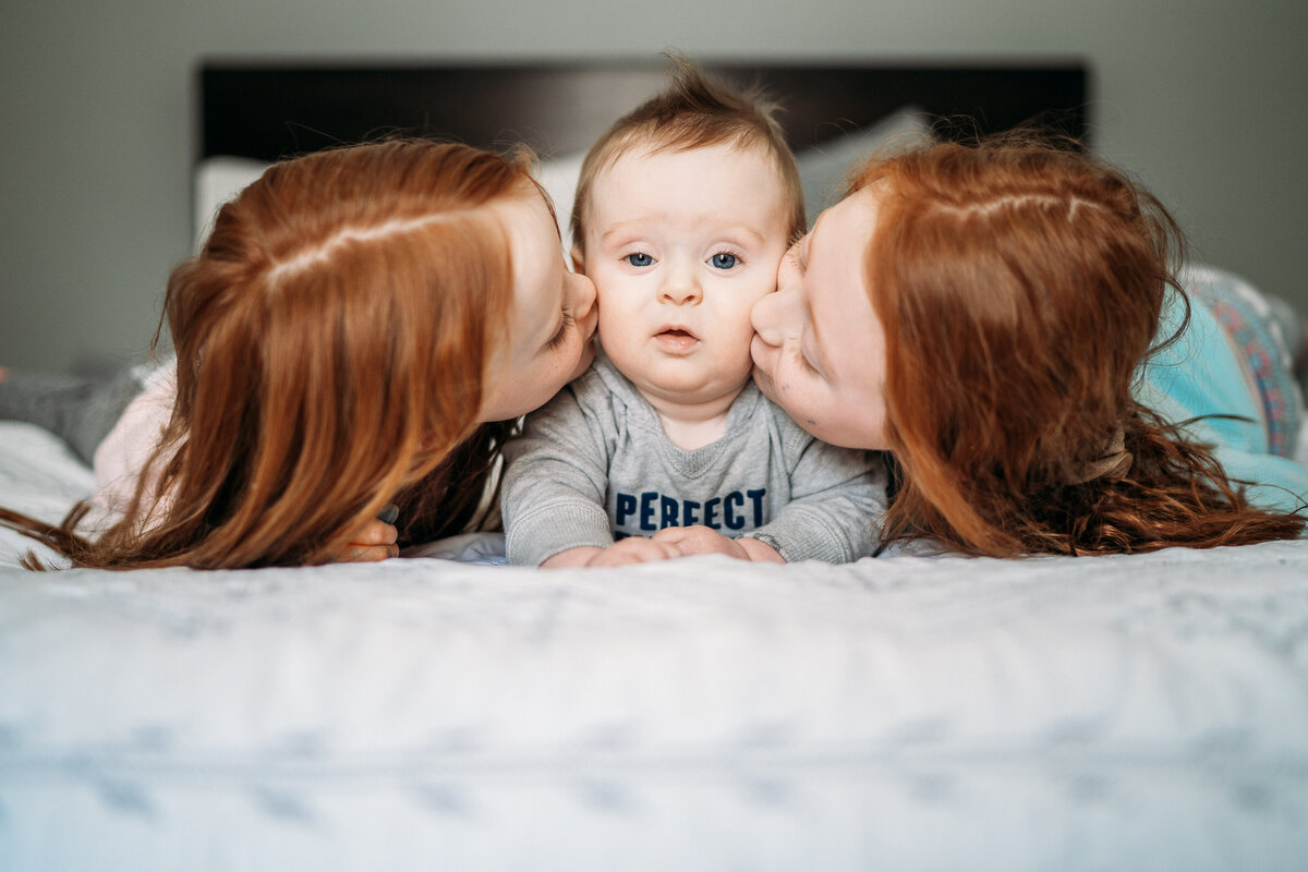 big sisters kissing baby brother on the cheek