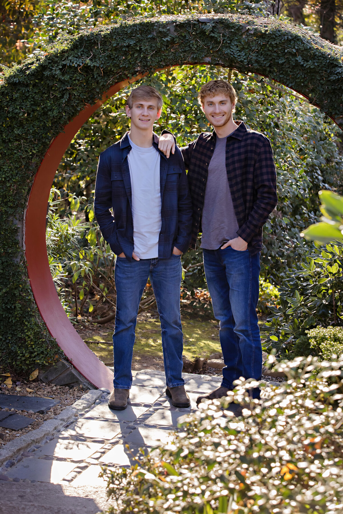 Lively portrait of two college‑age brothers standing together in moongate framed by autumn leaves at UNCC Botanical Garden Charlotte NC