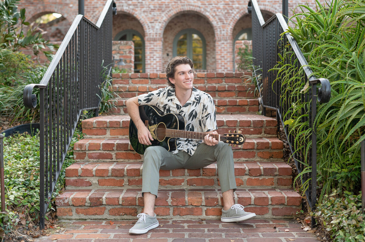 High school senior boy playing guitar on brick stairway.