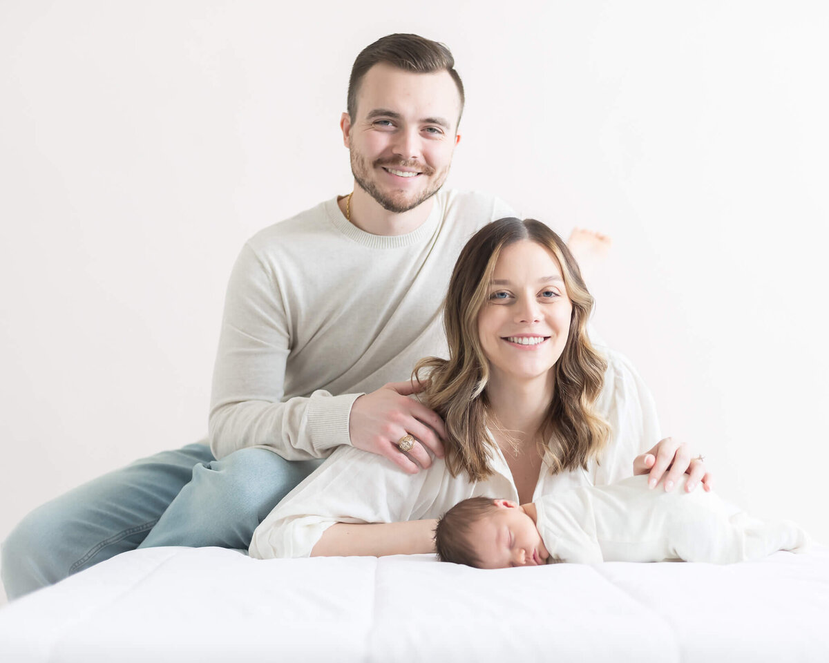 parents on bed with new baby smiling for portrait