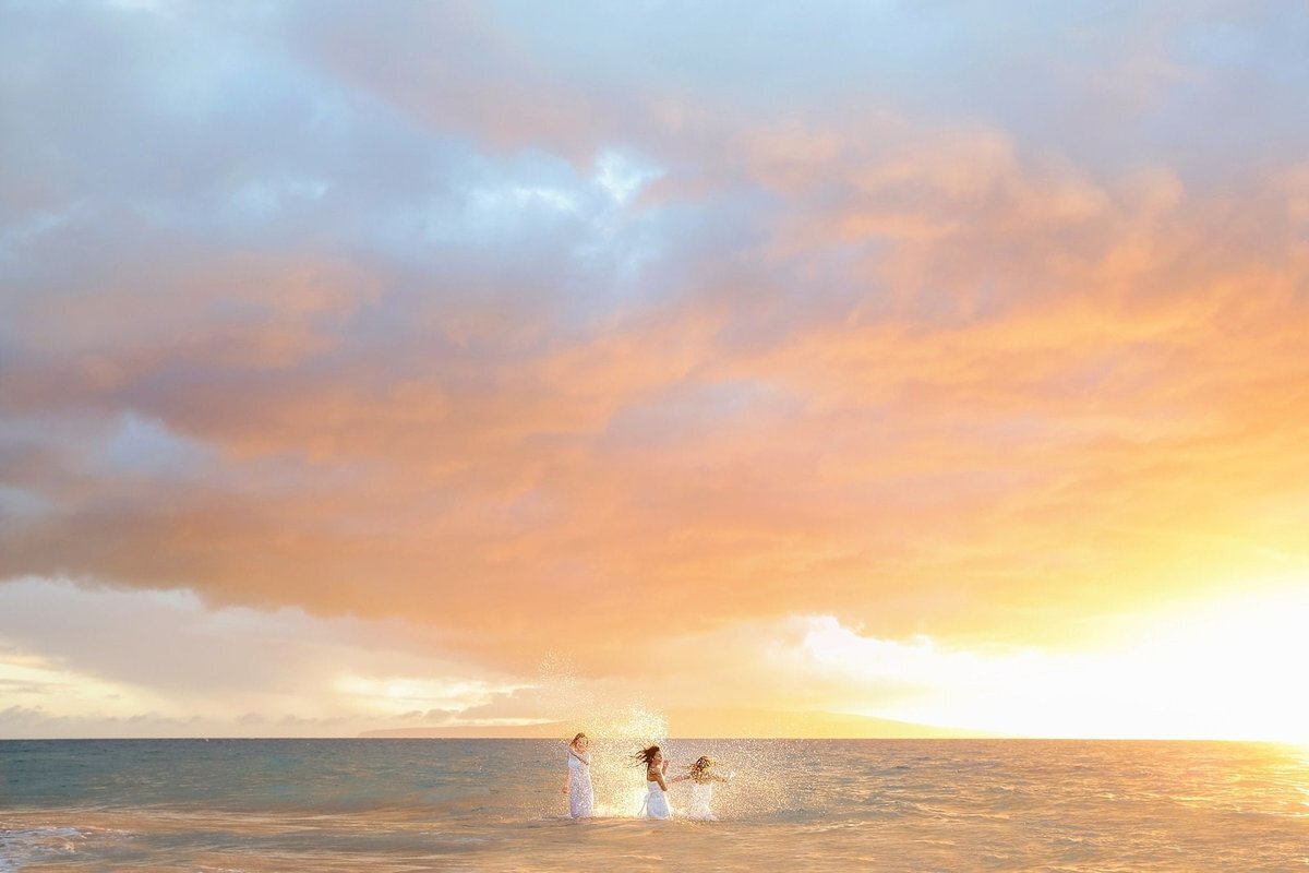 Three teen girls splash in the ocean off Maui at sunset