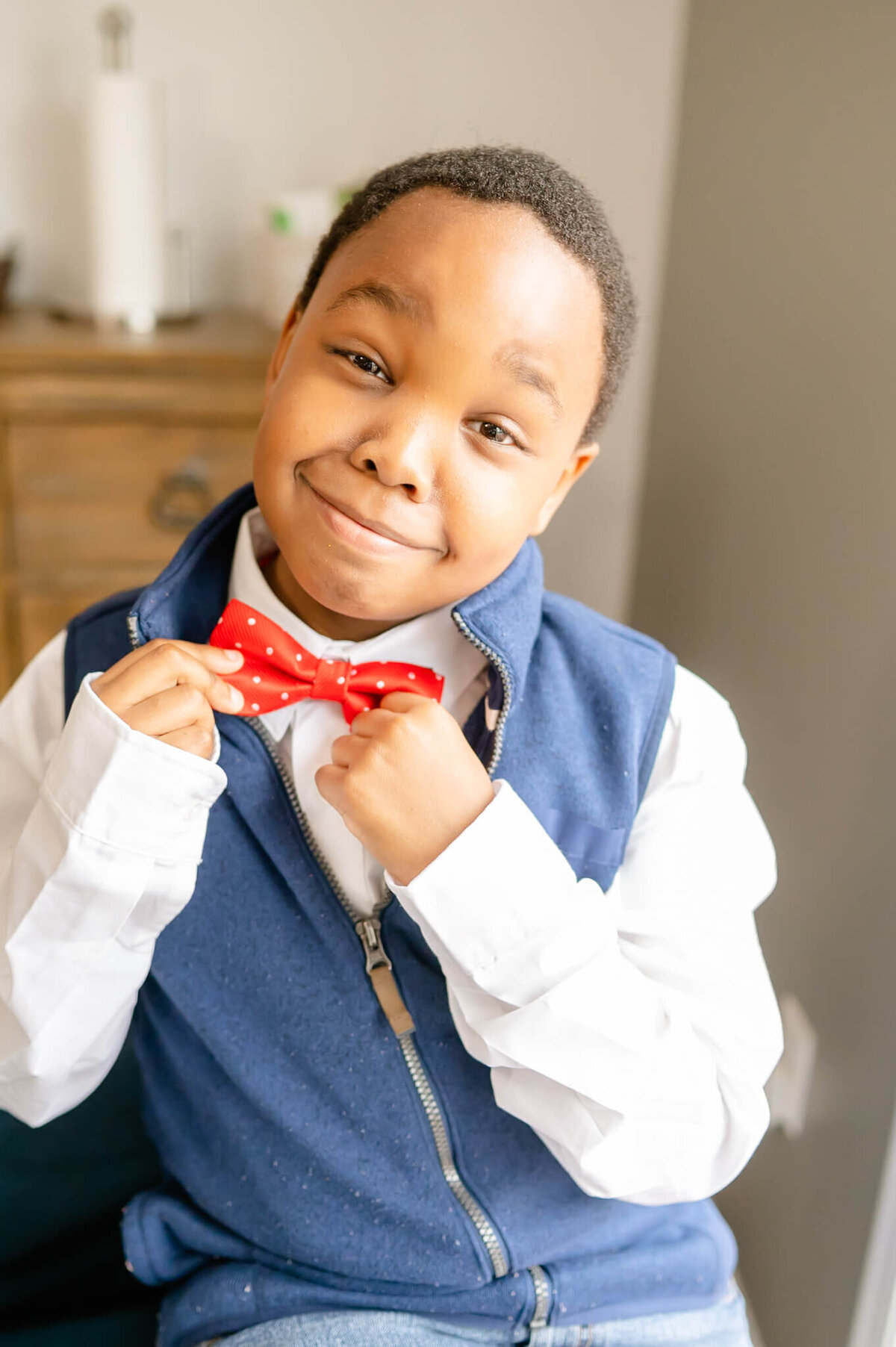 Young black boy fixing bowtie during in home family session near Chicago.