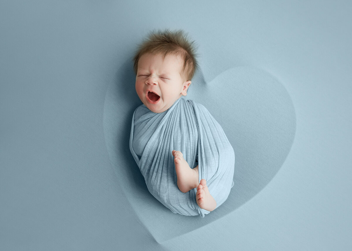 Newborn baby boy, wrapped in blue wrap laying in heart bowl during newborn photoshoot in Mount Juiliet Tennessee photography studio