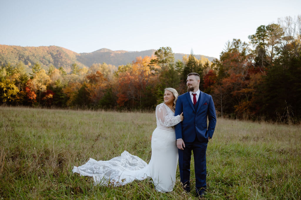 elopement photos of couple eloping to Gatlinburg at Cades Cove with bride holding grooms arm as they stand in a meadow in the moutnains at sunset 
