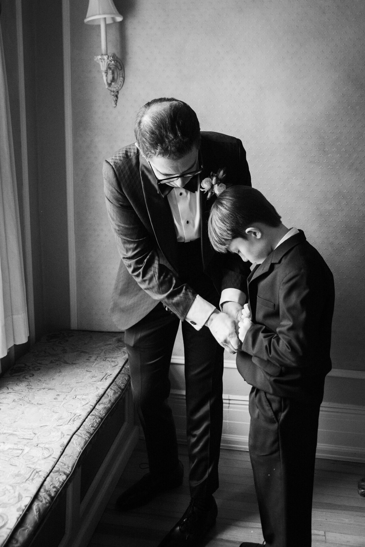 A candid moment of a groom helping the ring bearer with his suit.