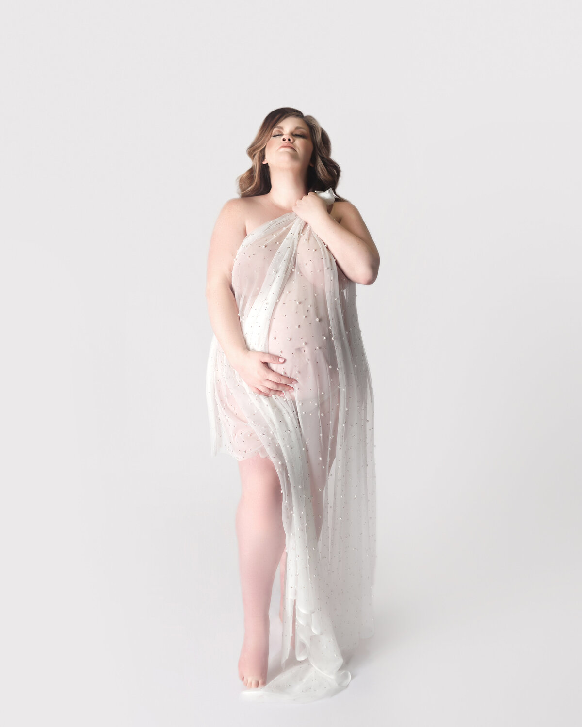 Pregnant women with white fabric draped over body during maternity photoshoot in Franklin Tennessee photography studio