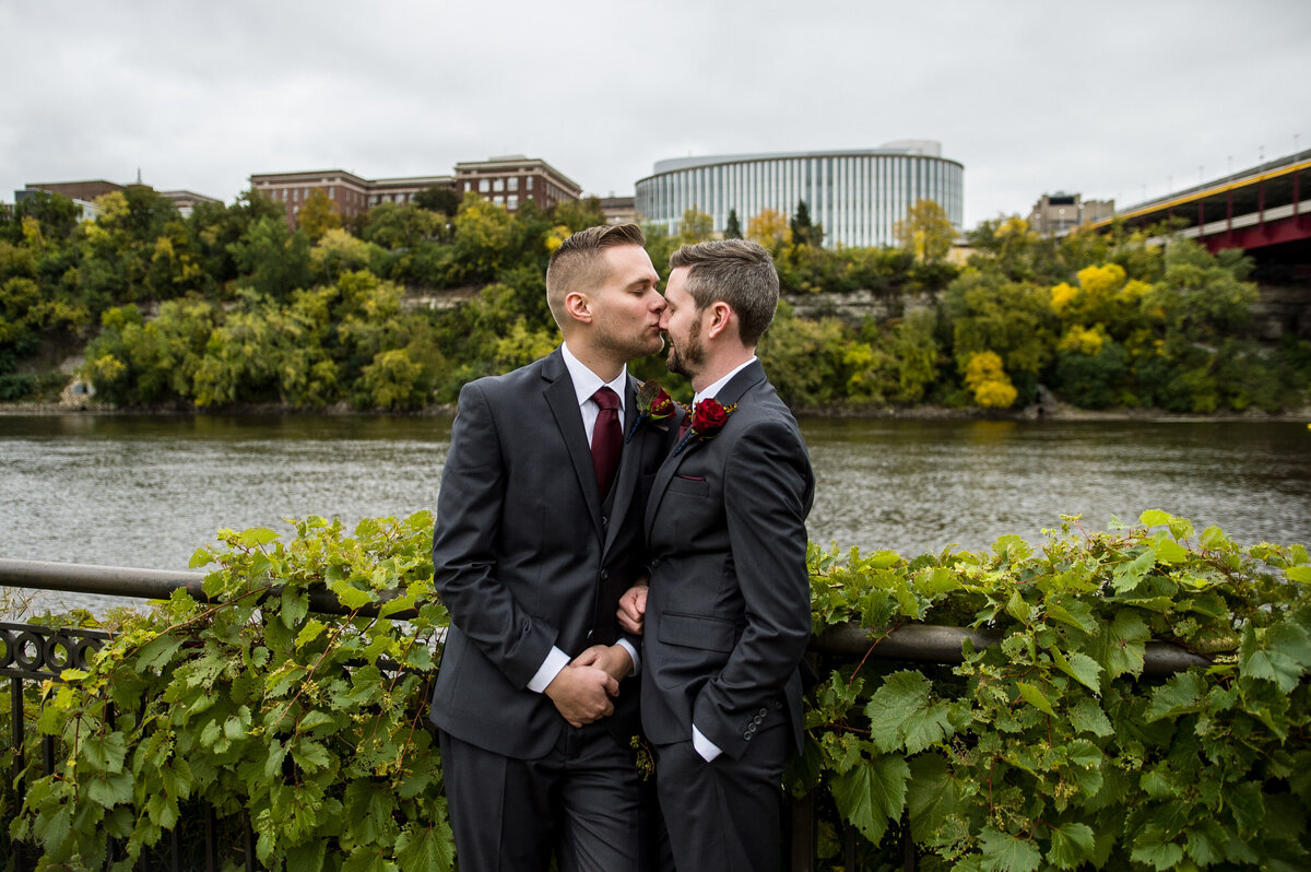 Groom kisses other groom on the nose in front of the river in Minneapolis, Minnesota.