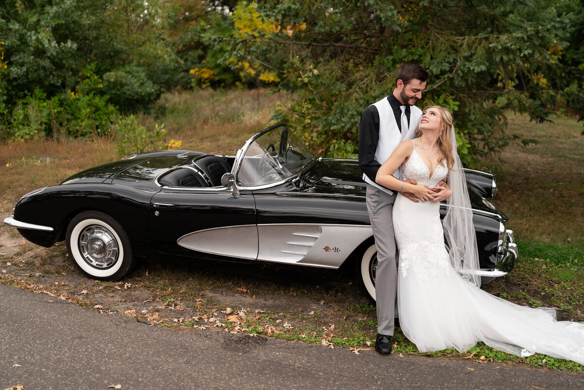Bride and groom smile in front of a vintage Corvette on their wedding day.