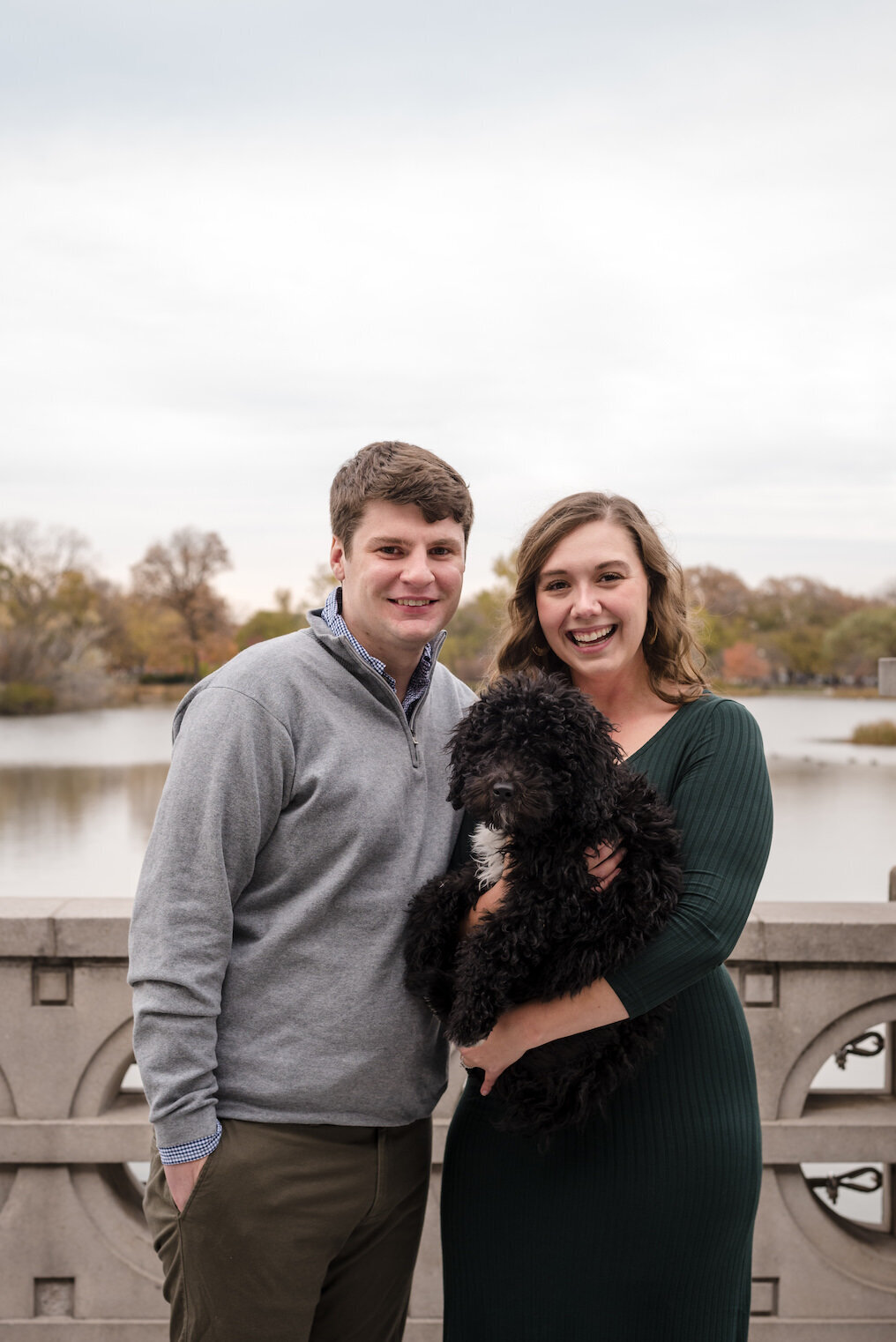 Couple smiles at the camera with their puppy at the Humboldt Park boathouse in Chicago, IL