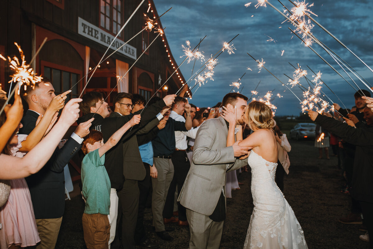 Bride and groom kissing in front of a crowd of people holding sparklers