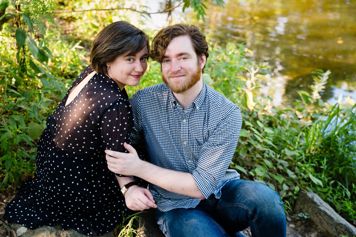 A couple sitting along the edge of a riverbank.