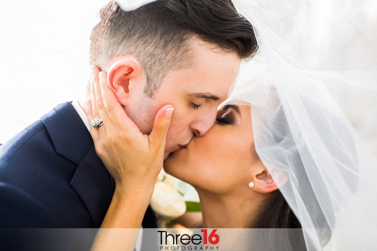 Bride and Groom share a very romantic kiss as the Bride holds his jaw while they are under her veil