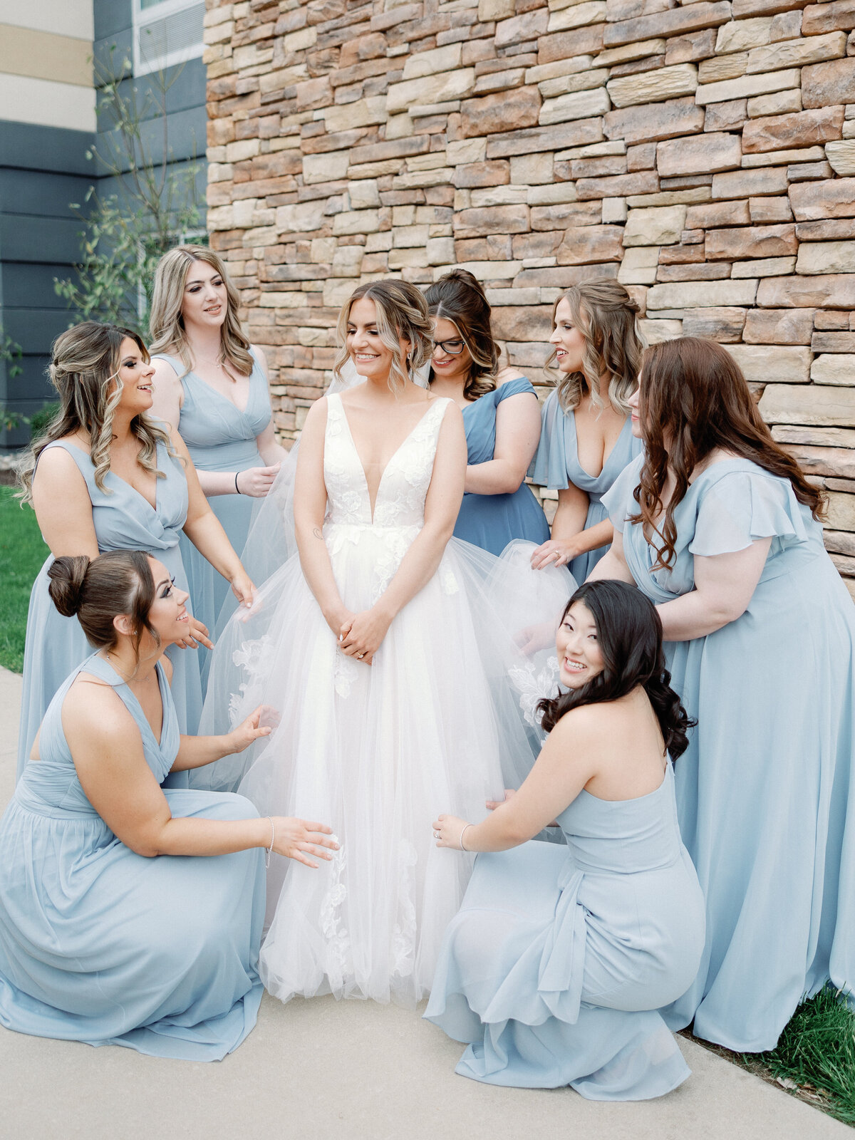A group if bridesmaids dressed in powder blue dresses all help the bride with her finishing touches to prepare for her ceremony