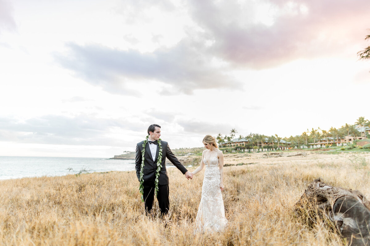 bride and groom holding hands on seaside cliffs with sunset