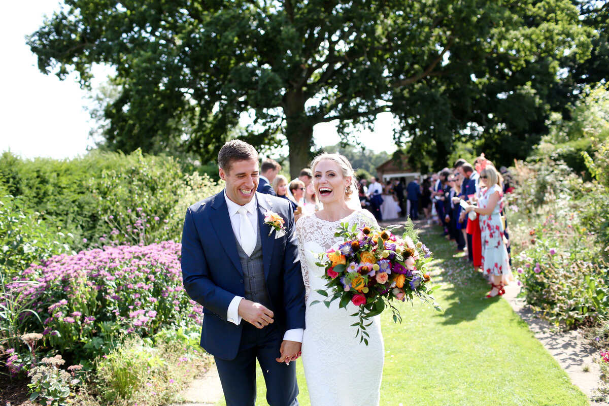 bride-and-groom-laughing-holding-flowers-at-luxury-wedding-in-hampshire