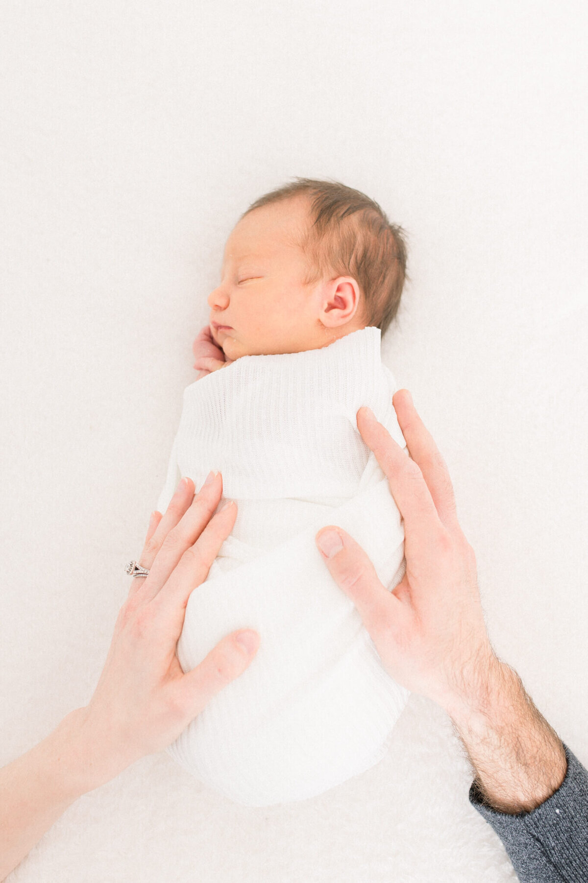 Parents hands in image toughing each side of baby while newborn sleeps captured by Niagara newborn photographer