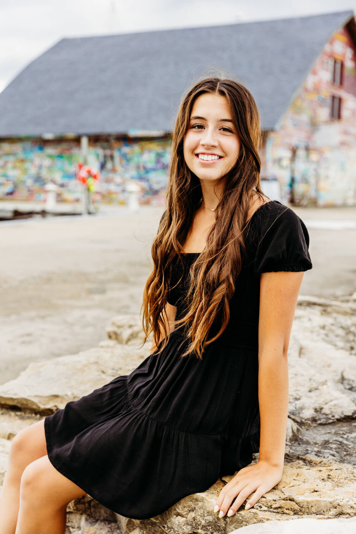 brunette teenage girl in a black dress sitting on a large rock near Oshkosh