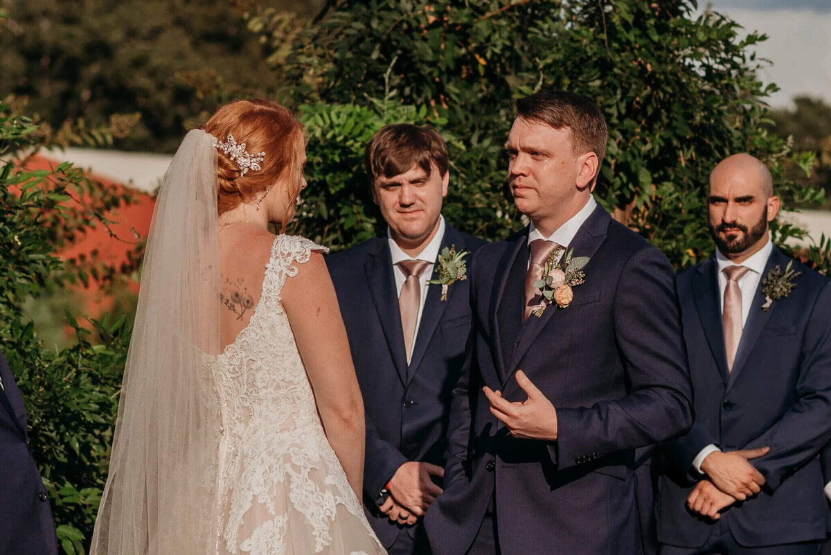 Photo of a groom crying in a navy suit Dearing a wedding ceremony outside
